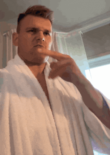 a man wearing a white robe is pointing at his nose