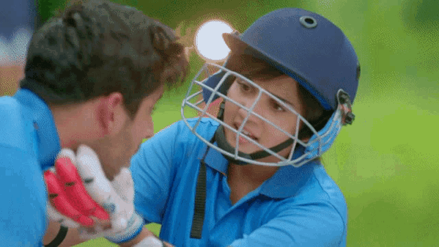 a man wearing a helmet talks to another man in a blue shirt