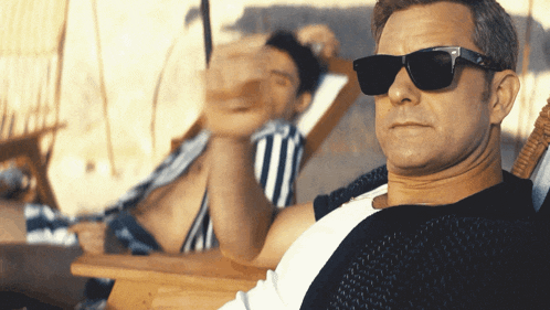 a man wearing sunglasses sits next to a woman in a striped bikini