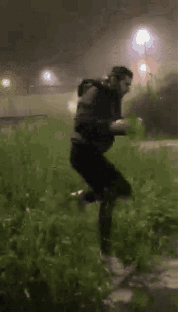 a man in a black jacket is running in the grass at night