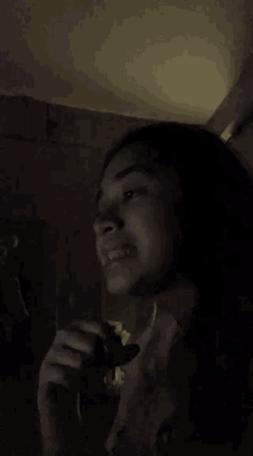 a woman is singing into a microphone in the dark while holding a cookie in her hand .
