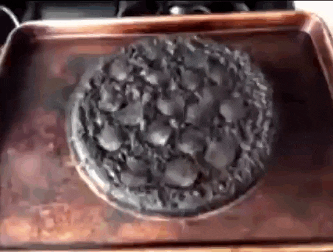 a burnt pizza is sitting on a wooden tray on a stove .