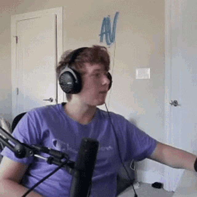 a young man wearing headphones is sitting in front of a microphone in a room .