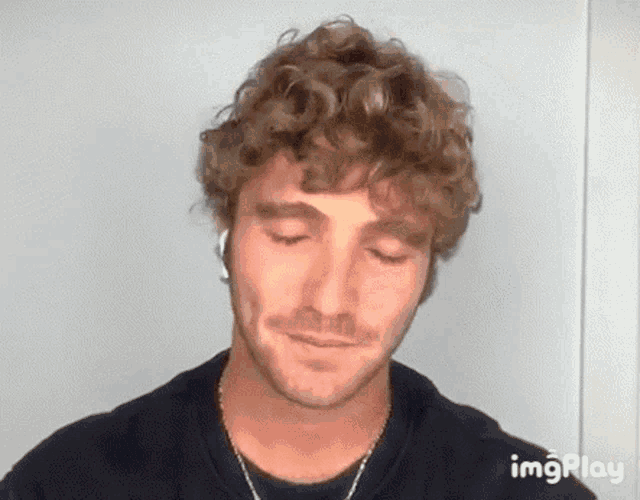 a man with curly hair is wearing headphones and a black shirt .