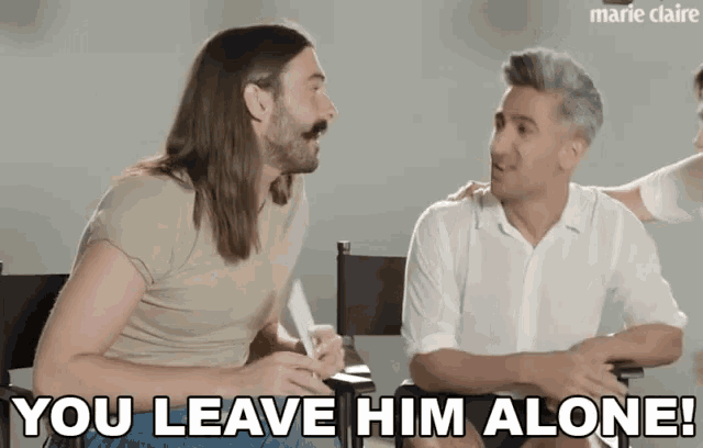 a man with long hair and a mustache is sitting next to another man and says you leave him alone