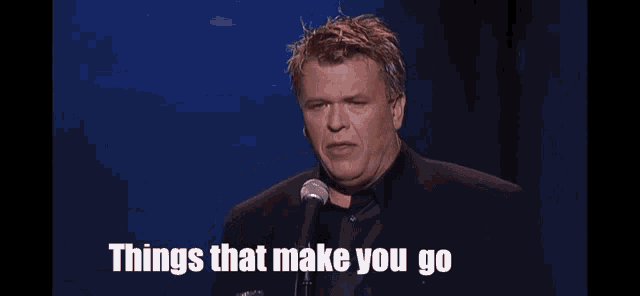a man is standing in front of a microphone holding a glass of water and saying things that make you go .