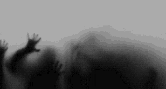 a blurred image of a person 's hands reaching out from behind a foggy glass wall .