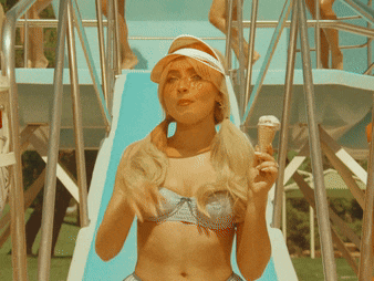 a woman in a bikini is holding an ice cream cone in front of a slide