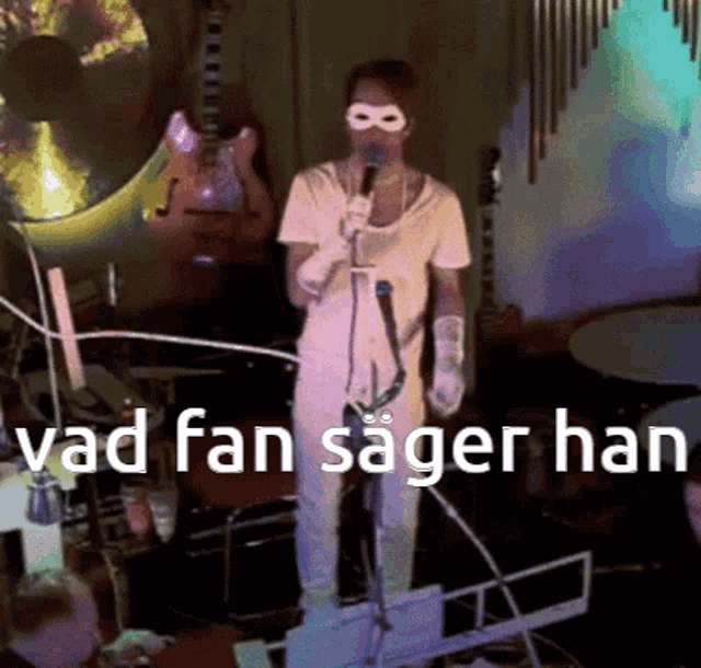 a man wearing a mask is singing into a microphone with the words vad fan sager han above him