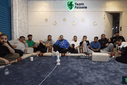a group of men sit on a couch in front of a sign that says team falcone