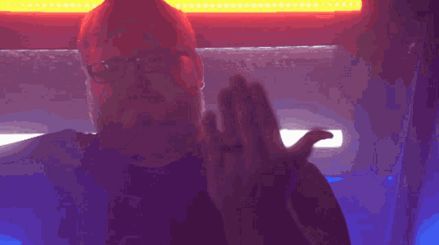 a man with glasses and a ring on his finger stands in front of a red light