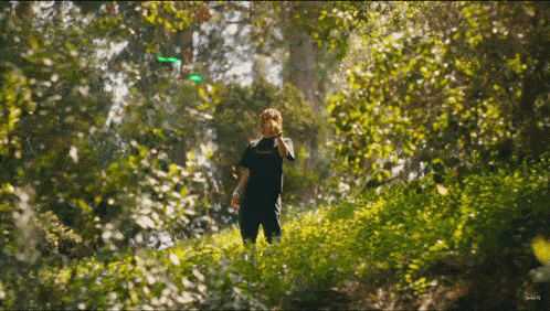 a man in a black shirt that says ' thrasher ' on it is standing in the woods