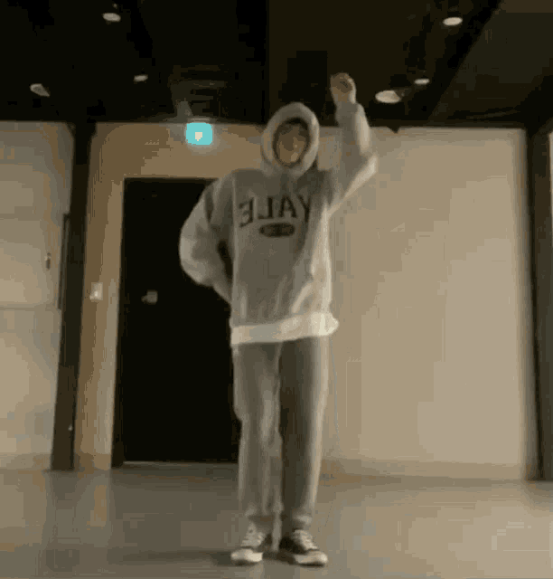 a man in a hoodie is standing in a room with his hands in the air .