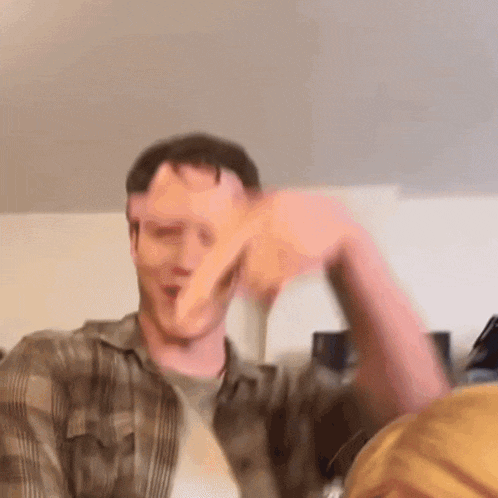 a man in a plaid shirt is making a funny face with his hand