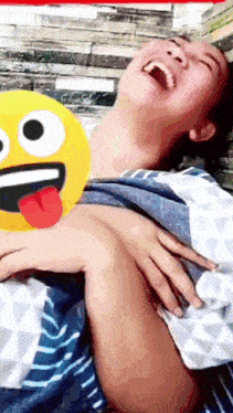 a woman is laughing while holding a yellow smiley face with her tongue out