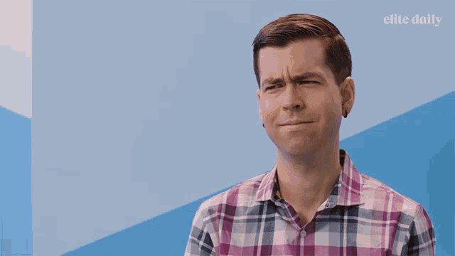 a man in a plaid shirt is making a funny face in front of a blue wall with elite daily written on it