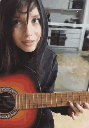 a girl in a black hoodie is holding a guitar
