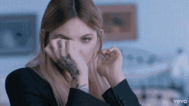 a woman with a tattoo on her hand is covering her eyes with her hands .