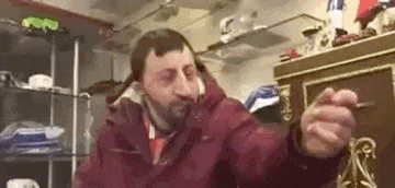 a man with a beard and a red jacket is holding a key in his hand in a room .