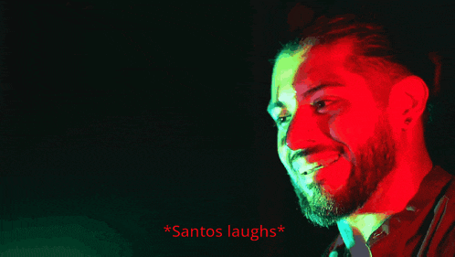 a man with a beard is smiling in a dark room with the words * santos laughs * below him