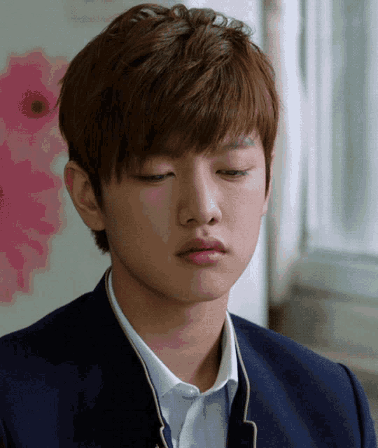 a close up of a young man 's face with a pink flower in the background