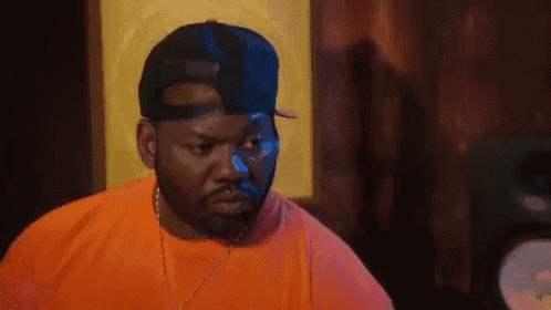 a man with a beard wearing an orange shirt and a black hat .