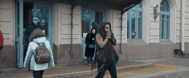 a man with dreadlocks is walking in front of a building with a sign that says 24