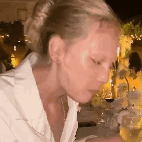 a woman in a white shirt is sitting at a table with wine glasses and flowers .