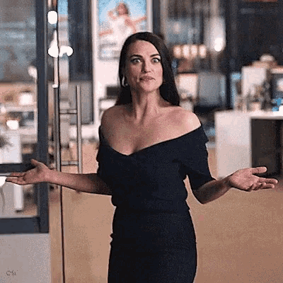 a woman in a black off the shoulder dress is standing in front of a glass door with her arms outstretched .