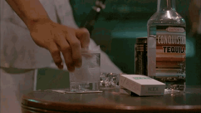 a bottle of conquista tequila is on a table next to a pack of cigarettes