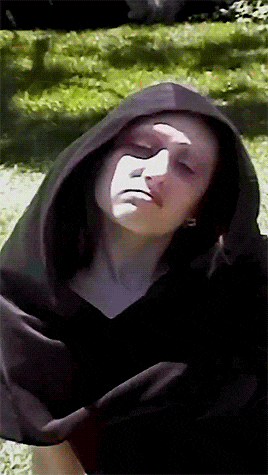 a woman wearing a black hooded cape looks down