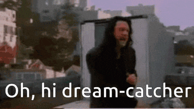 a man with long hair is standing in front of a building with the words `` oh , hi dream catcher '' .