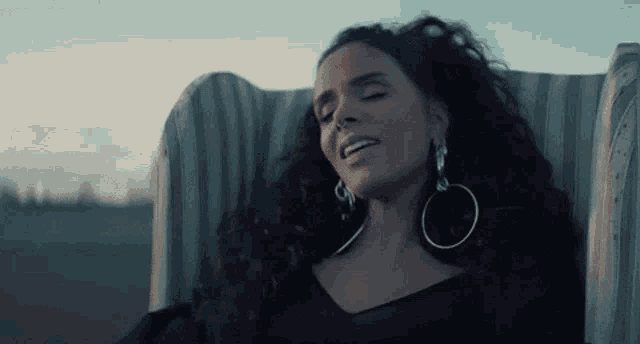 a woman with long dark hair is sitting in a chair with her eyes closed .