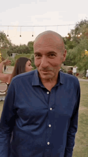 a man in a blue shirt is standing in a field with a woman in the background