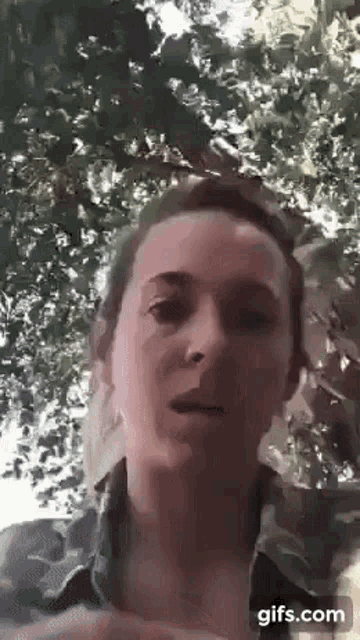 a woman is standing in front of a tree looking at the camera with a blurred background .