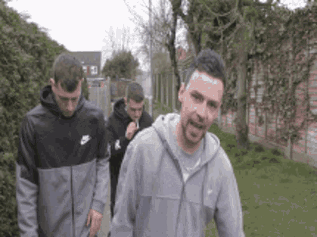 a man wearing a nike sweatshirt is walking with two other men