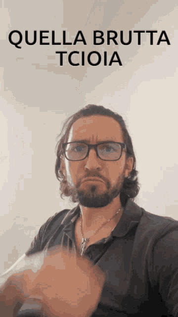 a man wearing glasses and a necklace is making a funny face with the words quella brutta tcioia behind him
