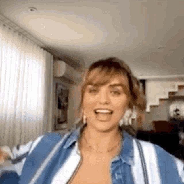 a woman is standing in a living room wearing a blue and white striped shirt and smiling .