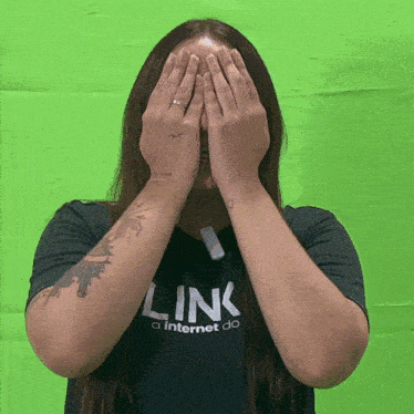 a woman wearing a black shirt that says link covering her face with her hands