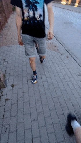a man wearing a t-shirt with palm trees on it walks down a sidewalk