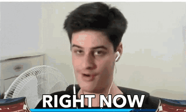 a man wearing ear buds is standing in front of a sign that says " right now "