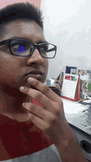 a man wearing glasses holds his hand to his chin in front of a calendar that shows the month of august