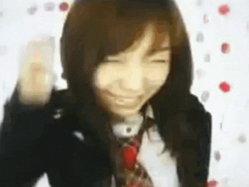 a woman in a school uniform and tie is smiling with her eyes closed and her fist in the air .
