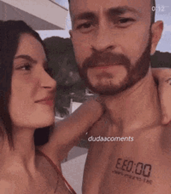 a man and a woman are posing for a picture with a tattoo on the man 's chest that says eeo 00