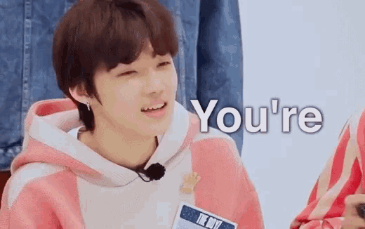 a young boy is wearing a pink and white hoodie and smiling while talking to someone .