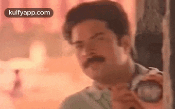 a man with a mustache is holding a camera in his hand and taking a picture .