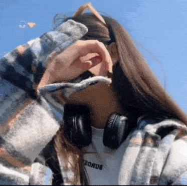 a woman wearing headphones and a plaid jacket has her hand on her face