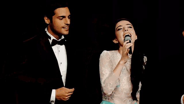 a man in a tuxedo sings into a microphone next to a woman in a white dress