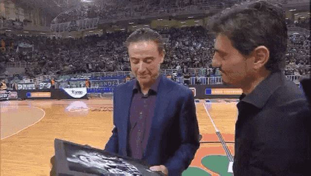 two men are standing on a basketball court looking at something
