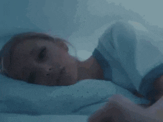 a woman is laying in bed with her head on a pillow with her eyes closed .